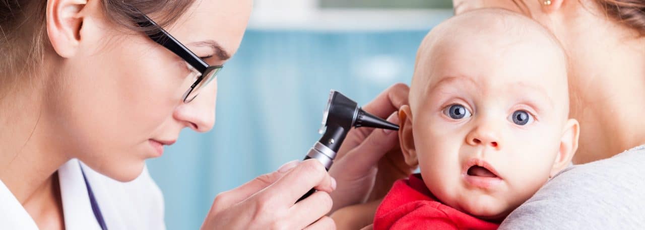 An audiologist using an otoscope to examine a child held by another adult