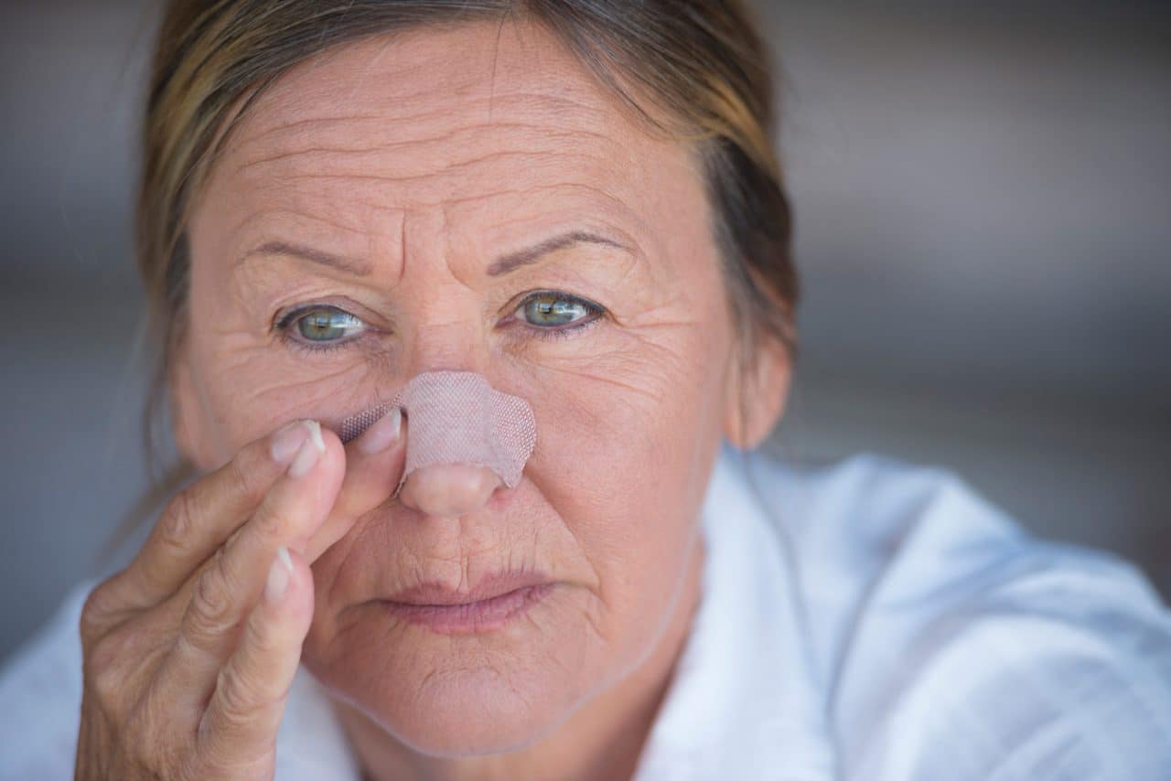 A person gently touching their nose, which has an adhesive bandage on it