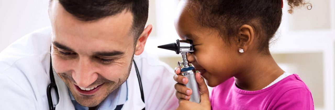 A child looking through an otoscope at a smiling audiologist