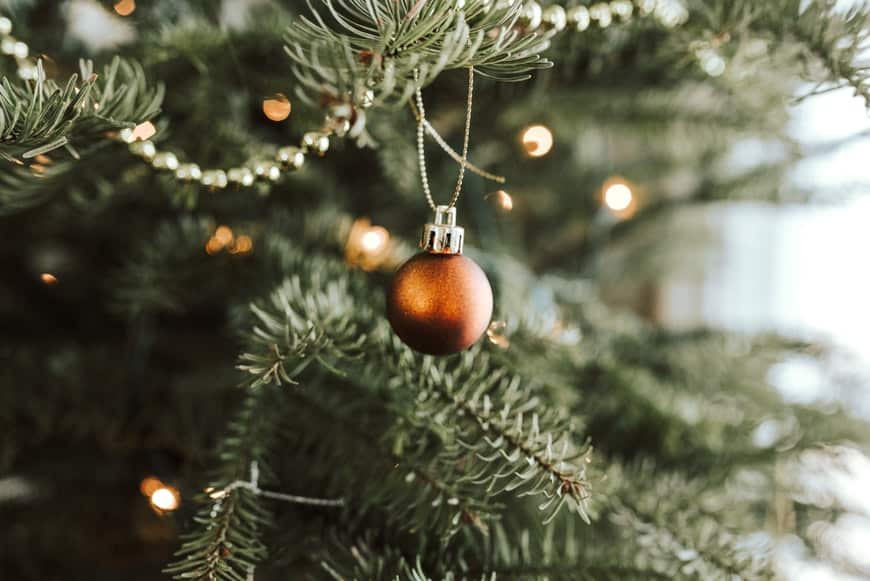 A traditional pine holiday tree with a red glass ornament.