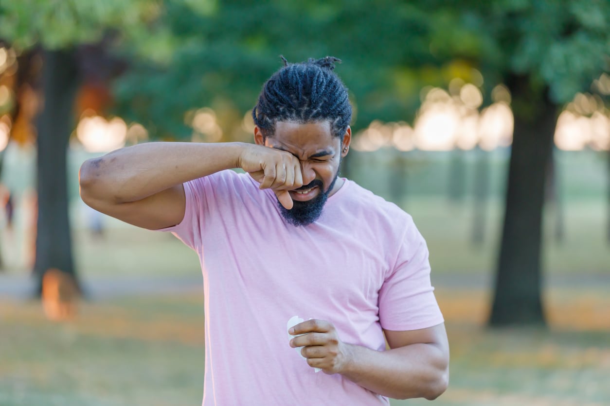 Man rubbing his itchy eye in the park.