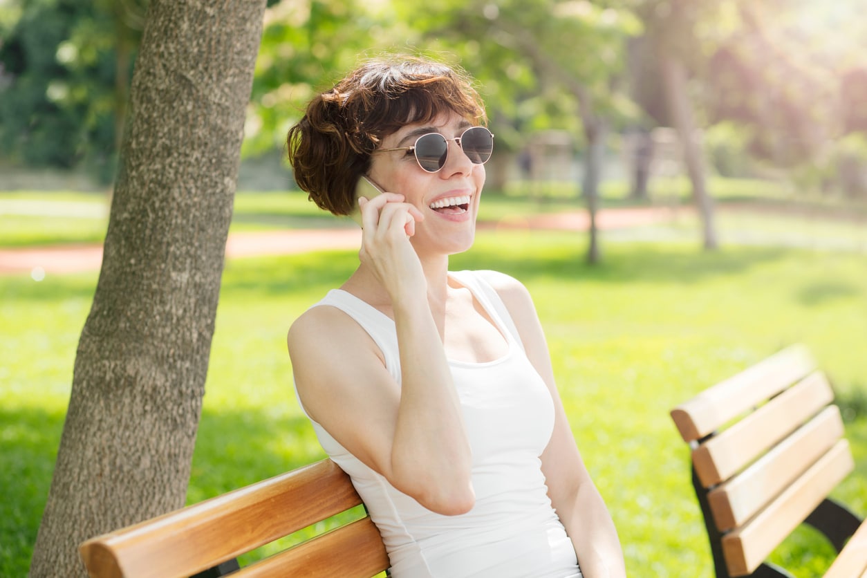 Happy woman talking on the phone on a bench in the park.