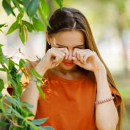 Woman standing next to a tree rubbing her eyes