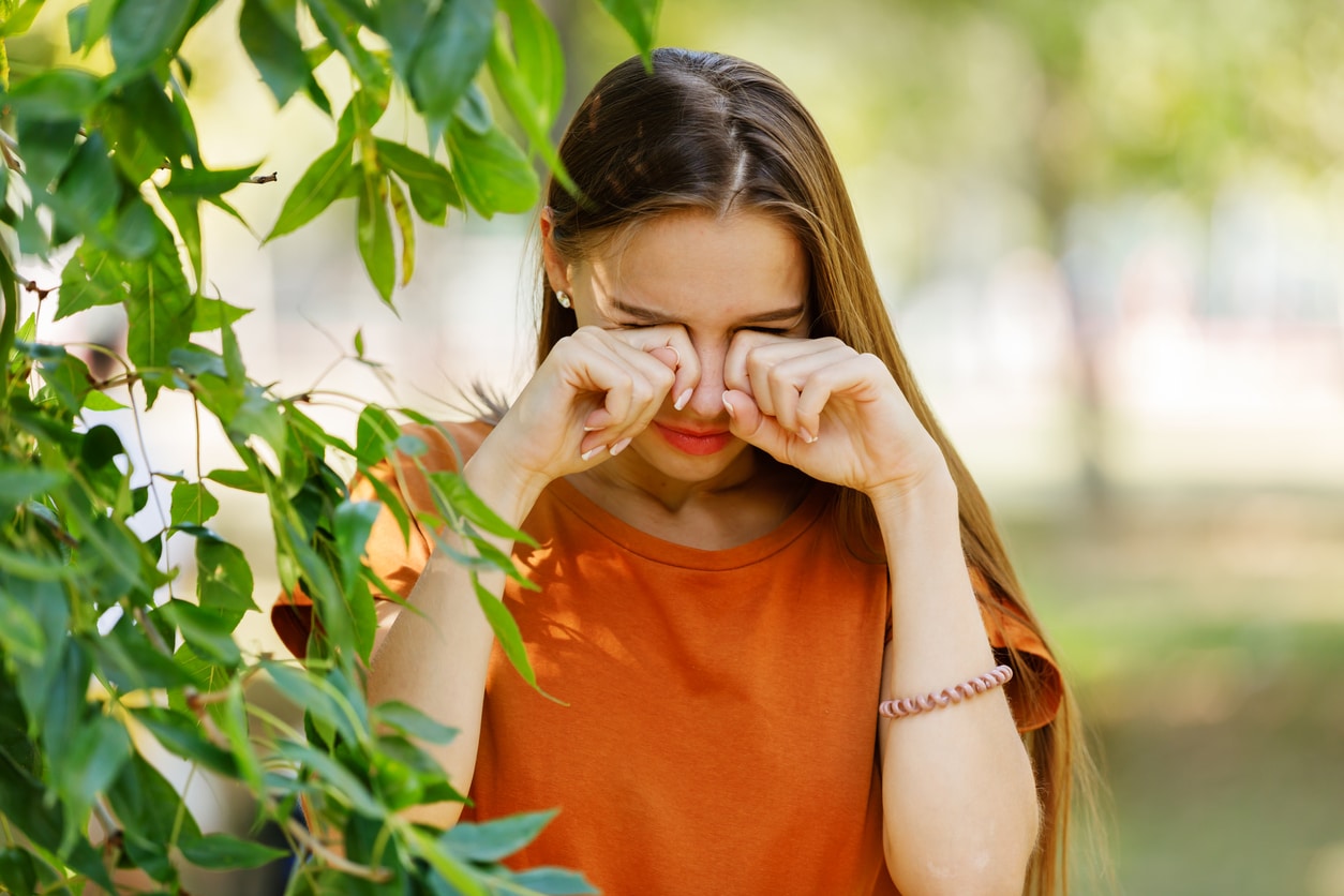 Woman standing next to a tree rubbing her eyes.