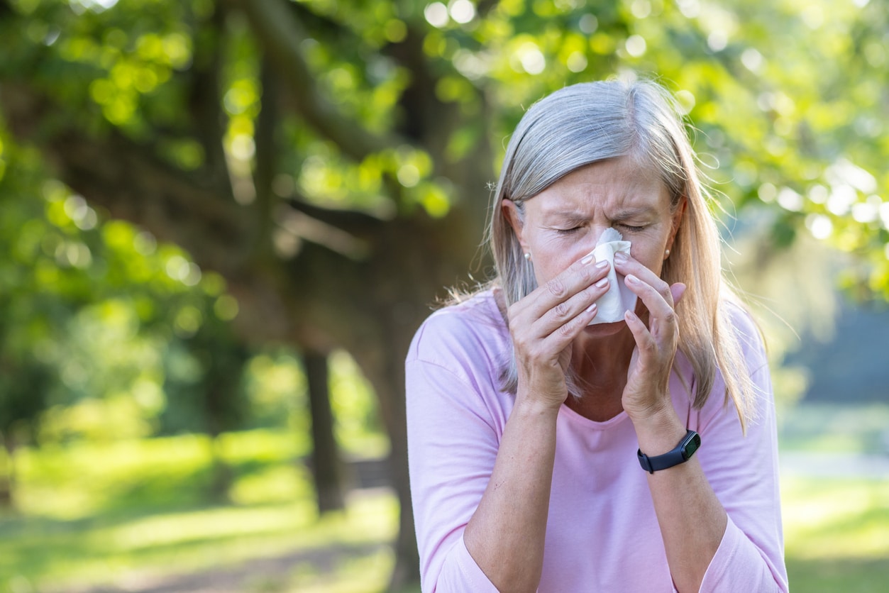 Senior woman sneezing at the park.