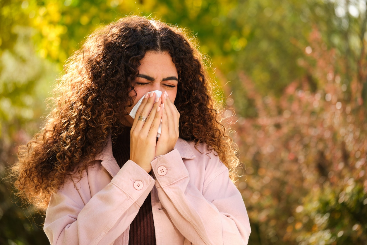 Woman with allergies blows nose in park