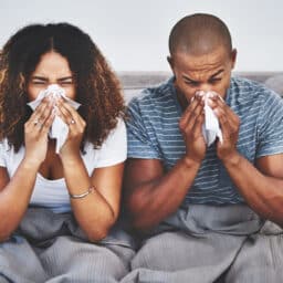A couple sneezing on the couch.