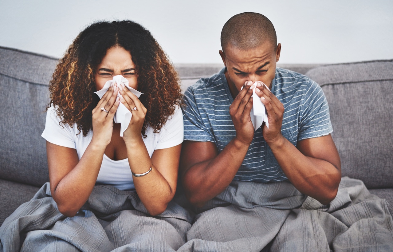 A couple sneezing on the couch.