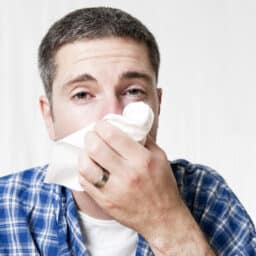 Man at home blowing his nose into a tissue